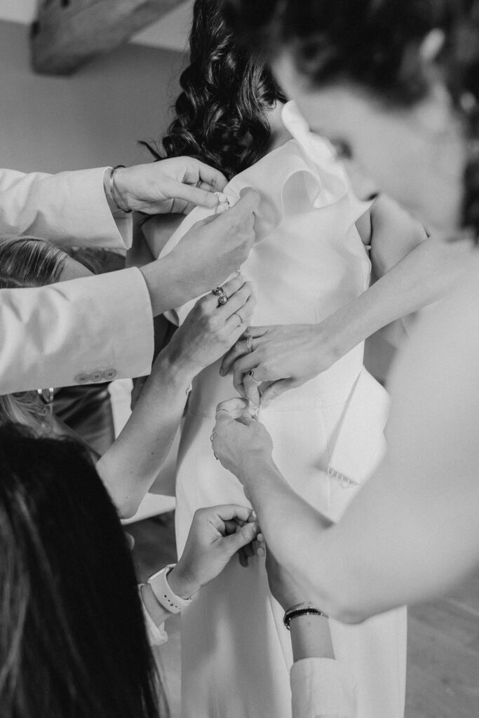 mains qui boutonnent la robe de la mariée lors de ses préparatifs