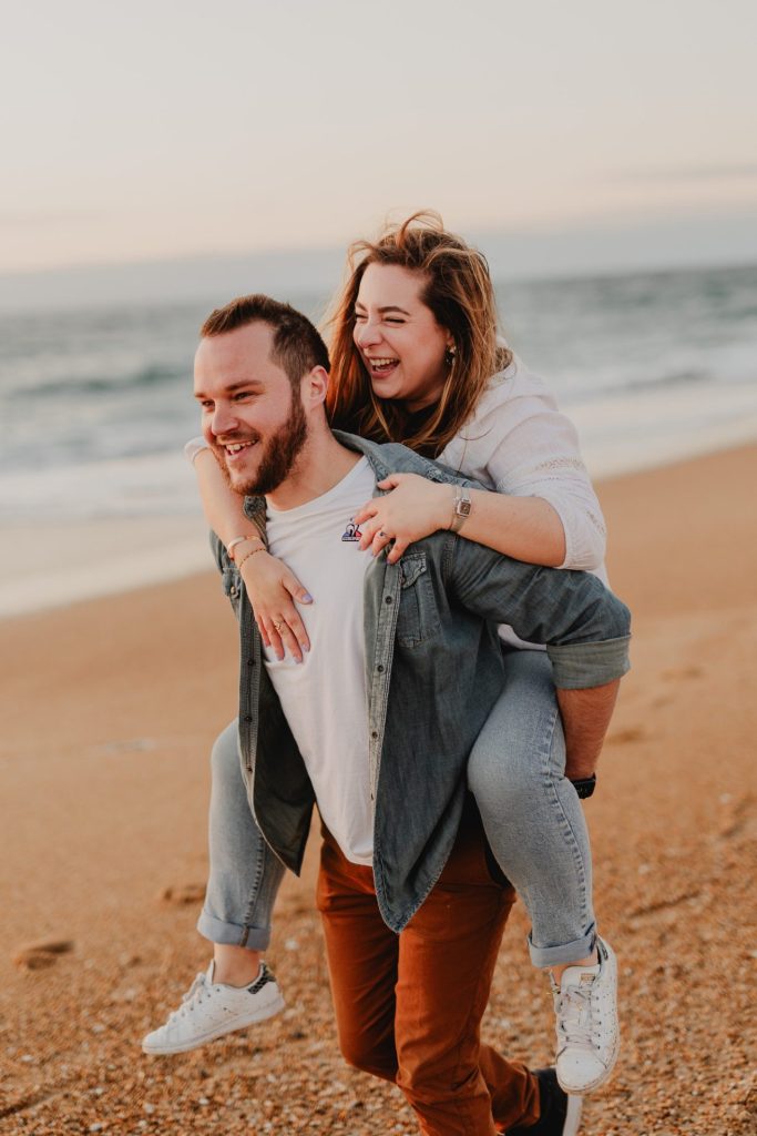 jeune femme saute sur le dos de son compagnon lors d'une séance photo de couple fun et amusante à Biarritz